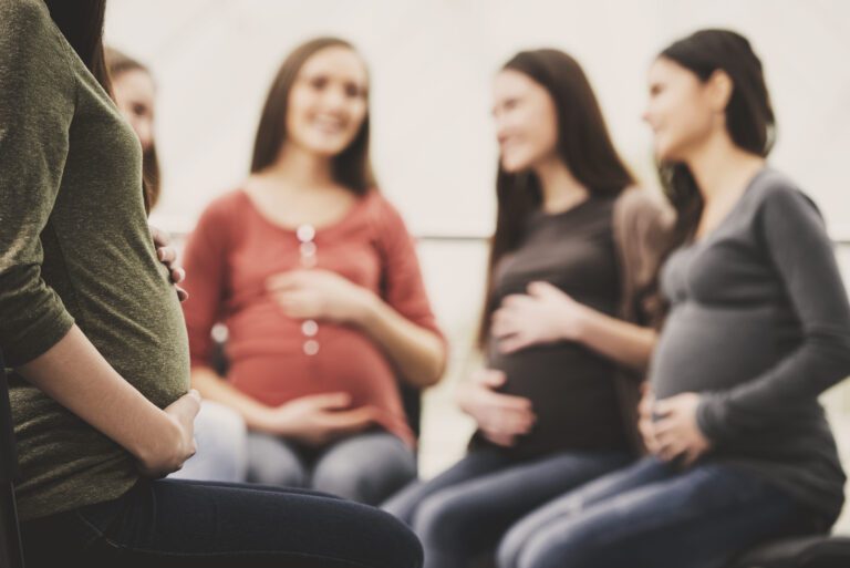 Pregnant girl holds onto stomach. Pregnant girls in background.