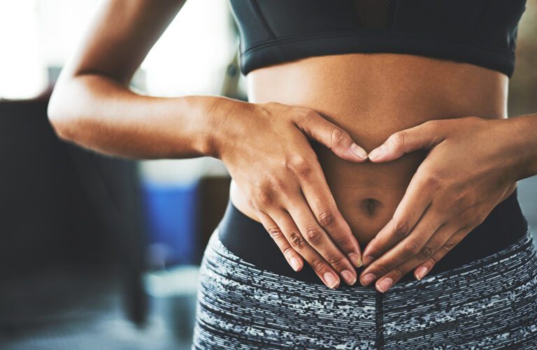 Cropped shot of a fit young woman making a heart shaped gesture over her stomach in a gym.