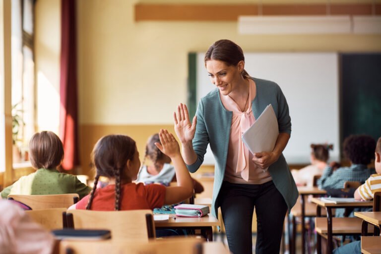 A teacher hi-fiving a female student in her classroom.
